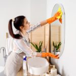 Young,Woman,Cleaning,Mirror,In,Her,Bathroom