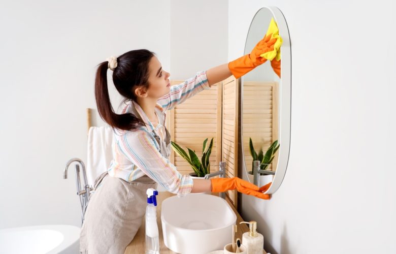 Young,Woman,Cleaning,Mirror,In,Her,Bathroom