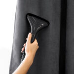 The,Girl,Holds,A,Steamer,For,Curtains,In,Her,Hand.